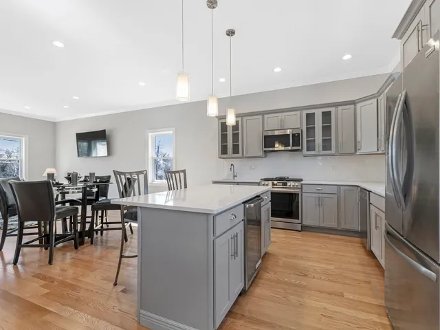 a kitchen with stainless steel appliances granite countertop a stove top oven a sink dishwasher a refrigerator and a dining table with wooden floor