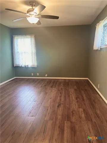 an empty room with wooden floor chandelier fan and windows