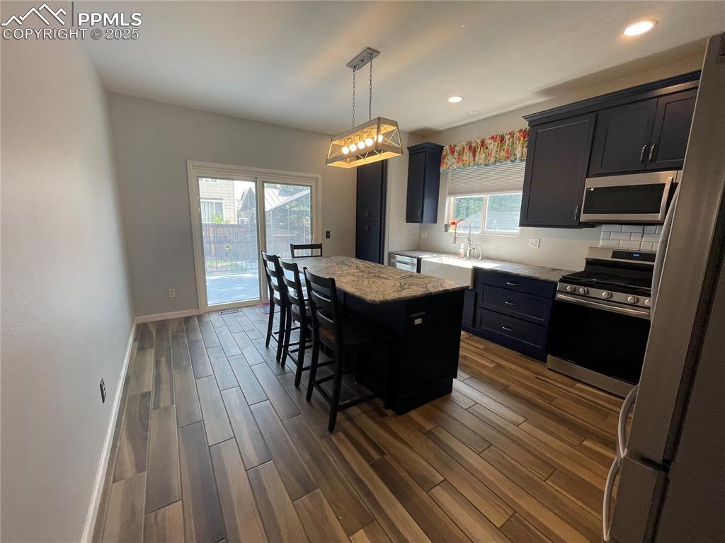 7631 Coffee Road Peyton, CO 80831 - Photo 7 of 28 a kitchen with stainless steel appliances granite countertop a stove a sink dishwasher a microwave oven and a dining table with wooden floor