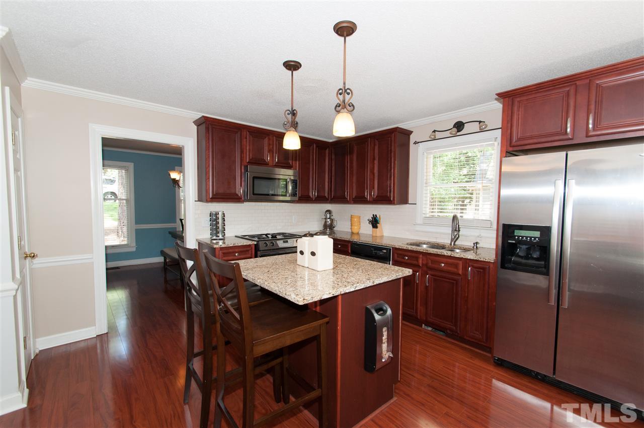 7304 Chicora Court Raleigh, NC 27615 - Photo 3 of 25 a kitchen with stainless steel appliances granite countertop a refrigerator a sink dishwasher a dining table and chairs with wooden floor