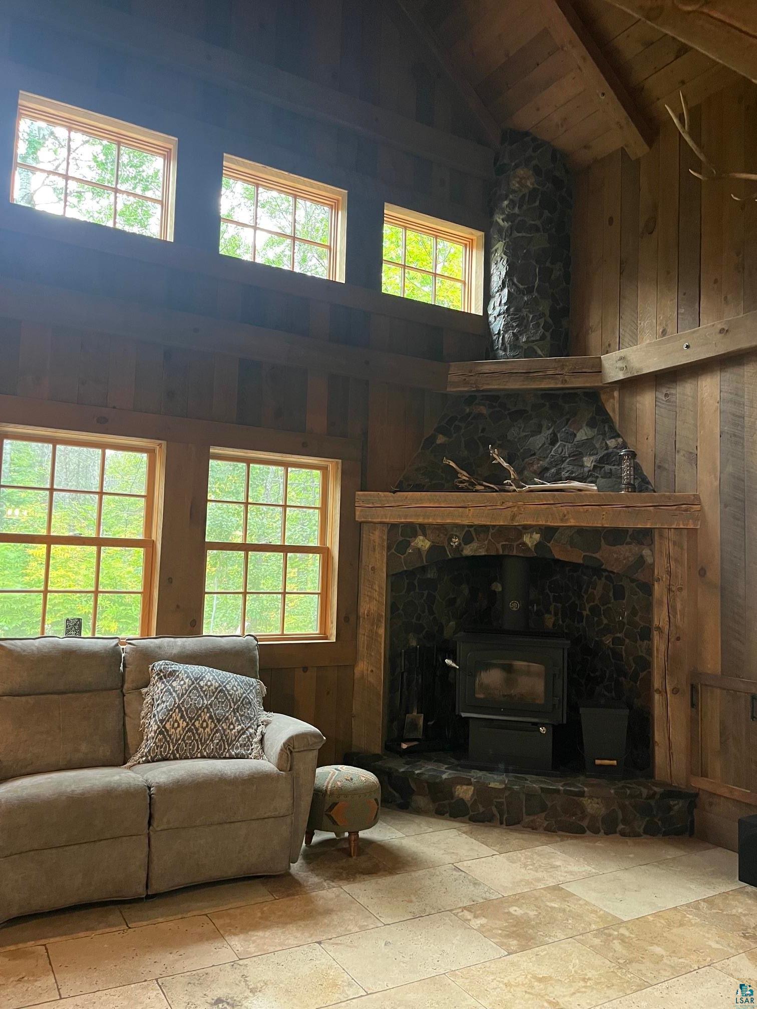 70745 Range Line Road Iron River, WI 54847 - Photo 10 of 40 Vaulted wood-paneled ceiling with exposed beams, stacked stone fireplace with wood-burning stove, multiple windows, and light-toned tile flooring