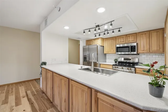 a kitchen with stainless steel appliances a sink dishwasher stove top oven and refrigerator with wooden floor