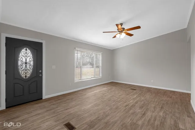 an empty room with wooden floor a ceiling fan and windows