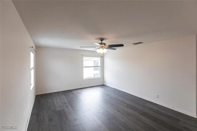 an empty room with wooden floor chandelier fan and windows