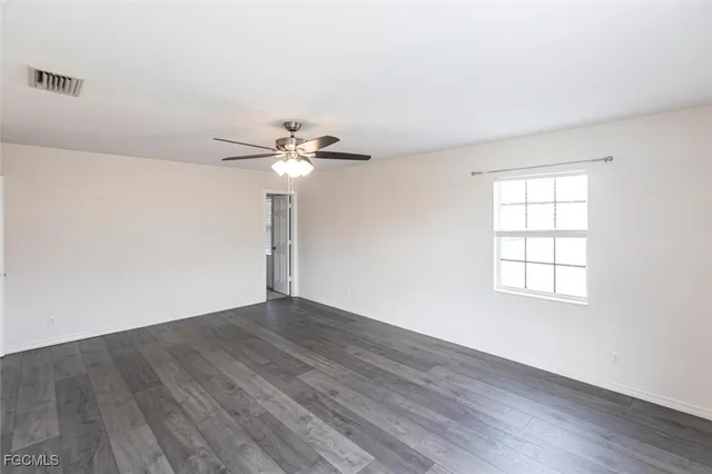 an empty room with wooden floor chandelier fan and windows