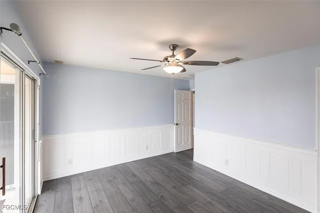 an empty room with wooden floor chandelier fan and windows