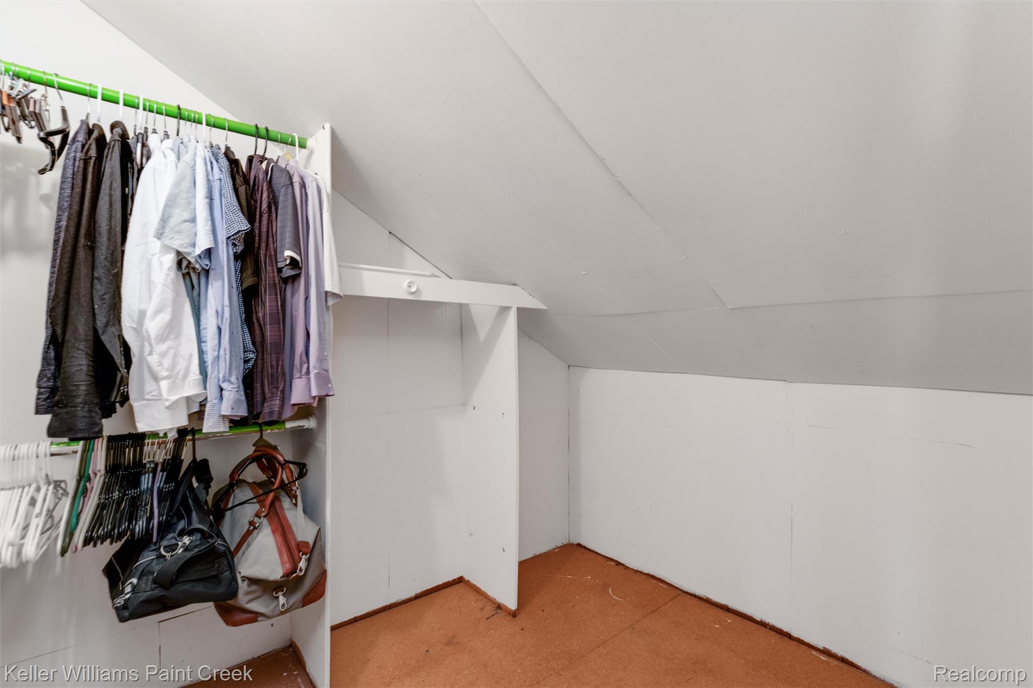 Sloped ceiling with white finish, built-in shelving, and hanging clothes racks