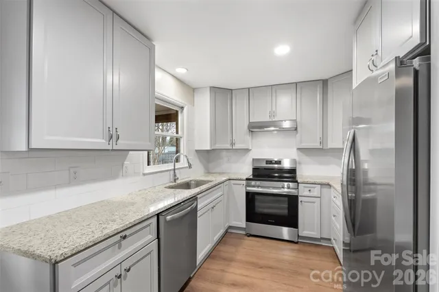 a kitchen with stainless steel appliances granite countertop a refrigerator a sink and white cabinets