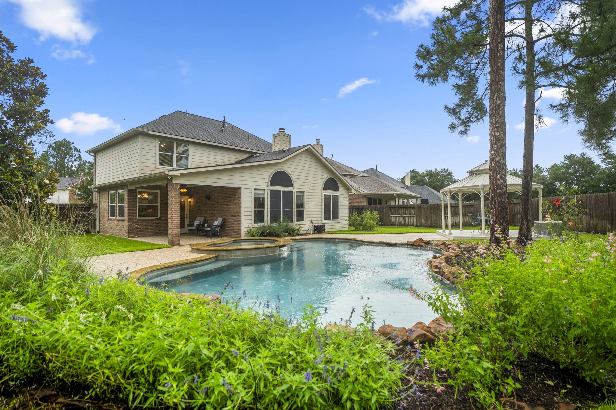 6311 Sparrows Glen Lane Spring, TX 77379 - Photo 37 of 50 Framed by wildflower plantings and mature trees, this view captures the backyard at its best—pool + spa, covered patio, gazebo, and a layered landscape that gives the entire space a refined resort feel.