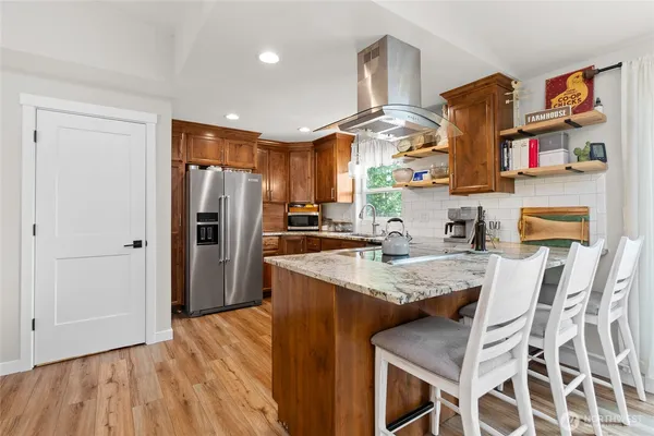 a kitchen with stainless steel appliances granite countertop a refrigerator a sink dishwasher a stove and a dining table with wooden floor