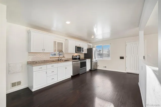 a large white kitchen with granite countertop a stove top oven a sink dishwasher and white cabinets with wooden floor