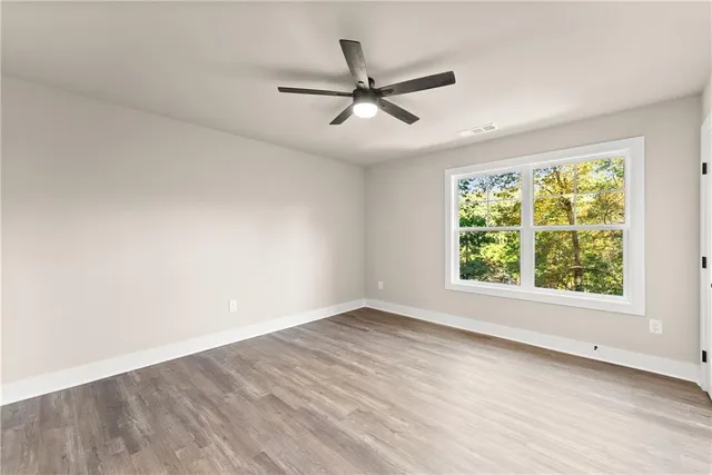 an empty room with wooden floor fan and windows