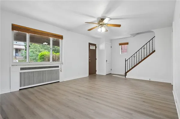 a view of an empty room with wooden floor and fan