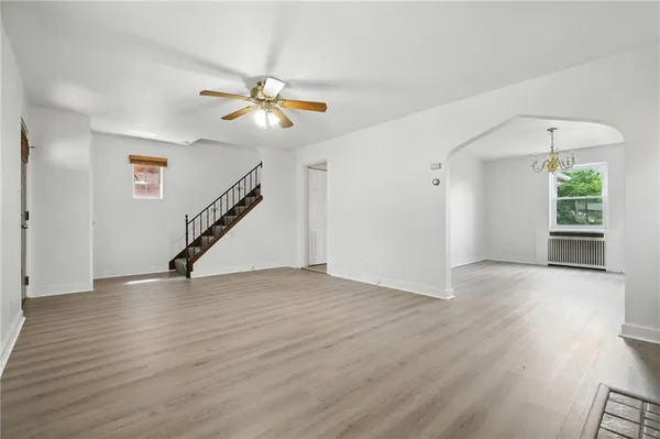 a view of an empty room with wooden floor and a ceiling fan
