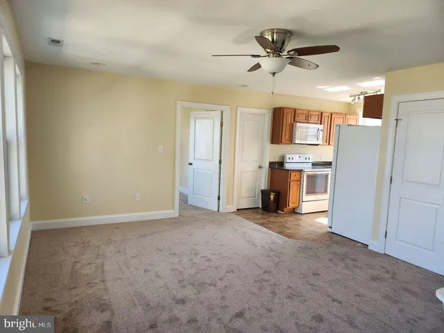 a view of a livingroom with a fireplace a ceiling fan a kitchen space a sink a refrigerator a ceiling fan and closet