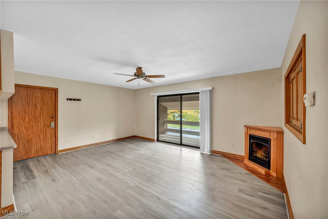 1263 Lost Nation Road, Unit 5 Willoughby, OH 44094 - Photo 6 of 26 Unfurnished living room featuring a glass covered fireplace, light wood finished floors, a ceiling fan, and a textured ceiling