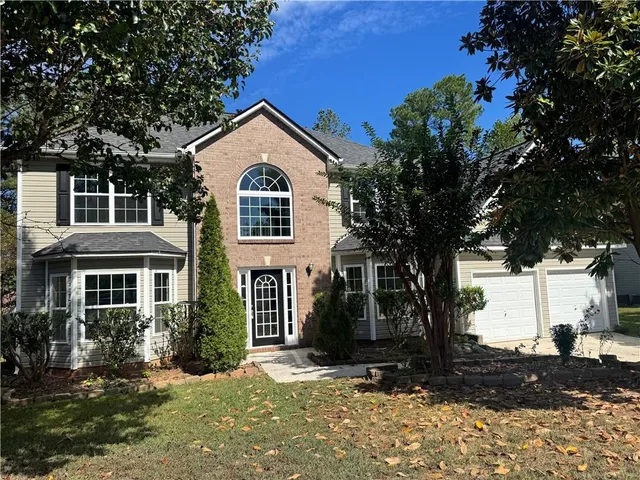 a view of a white house next to a yard with large trees