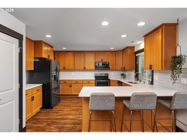 a kitchen with stainless steel appliances kitchen island granite countertop a refrigerator a stove top oven and a dining table with wooden floor