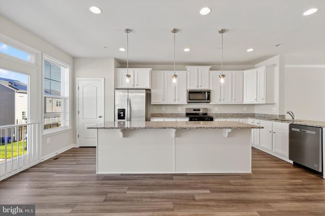 a large kitchen with stainless steel appliances granite countertop a stove a sink a refrigerator and white cabinets with wooden floor