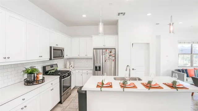 a an open kitchen with stainless steel appliances kitchen island granite countertop a refrigerator a sink dishwasher and white countertops with wooden floor