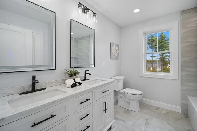 a bathroom with double sink a toilet a and a window