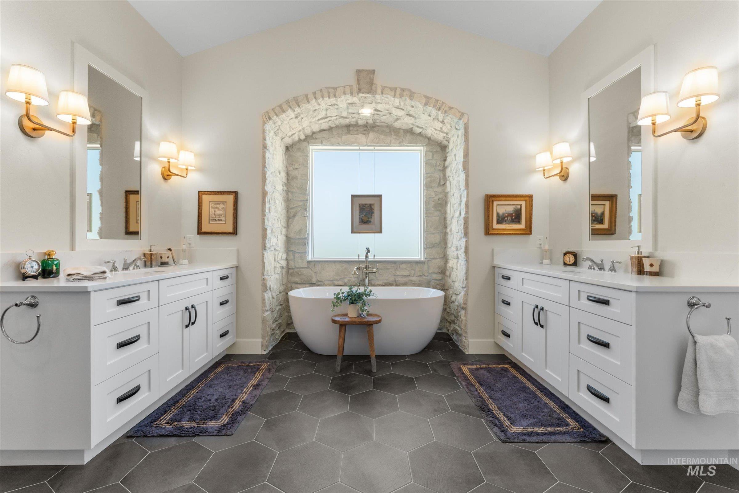 6585 South Pemberley Way Meridian, ID 83642 - Photo 25 of 43 Spacious bathroom featuring a freestanding tub within a stone archway, dual white vanities with quartz countertops, hexagonal floor tiling, and wall-mounted sconces