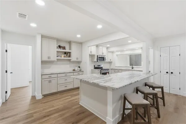 a large white kitchen with a lot of counter space and wooden floor