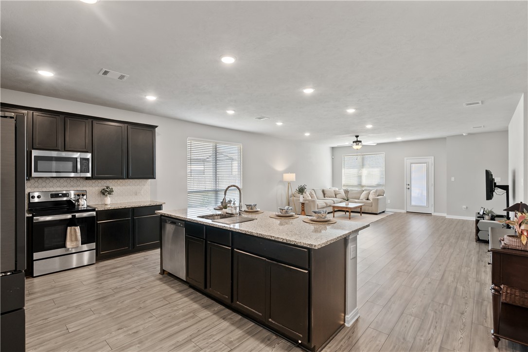 1925 Viva Road Bryan, TX 77807 - Photo 22 of 25 Kitchen with stainless steel appliances, open floor plan, a kitchen island with sink, light stone countertops, and recessed lighting