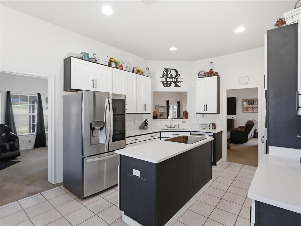 130 Parsonage Street Azle, TX 76020 - Photo 7 of 39 Two tone kitchen with stainless steel fridge, a center island, dual tone cabinetry, light colored carpet, and recessed lighting