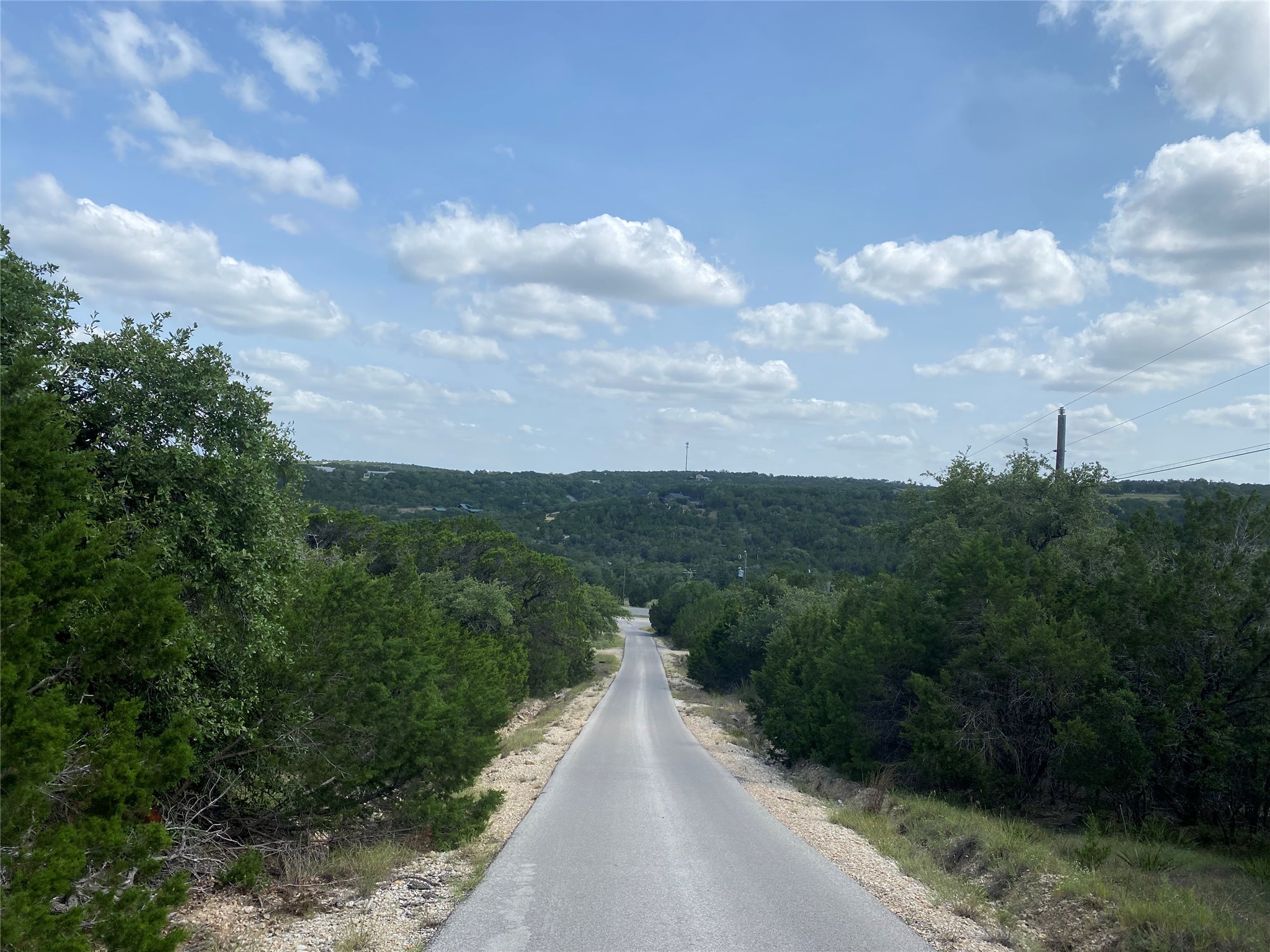 Tbd Whisper Ridge Wimberley, TX 78676 - Photo 6 of 7 A private paved road winds through a lush, green landscape, offering serene hillside views.