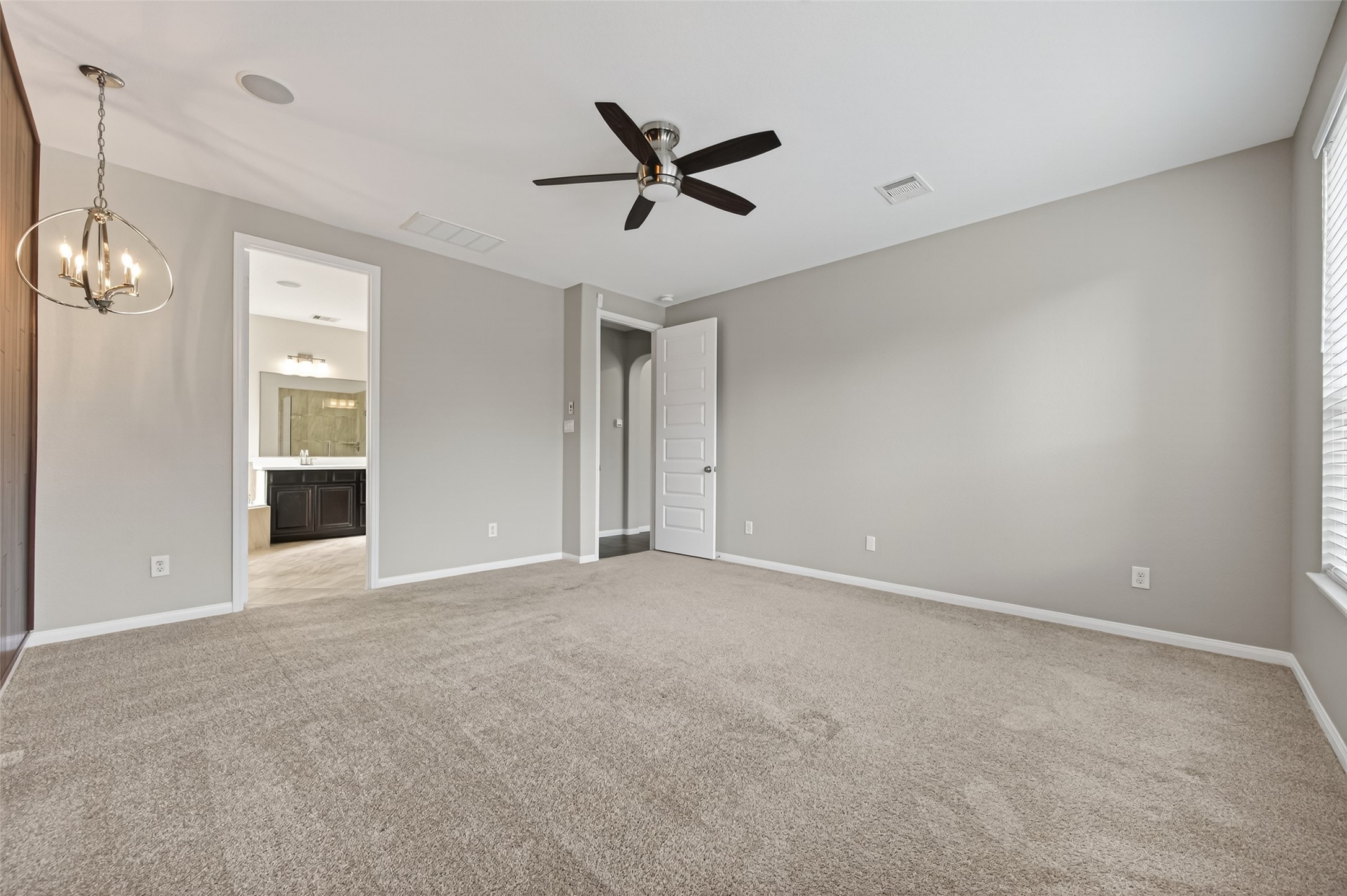 7003 Bristol Memorial Drive Spring, TX 77379 - Photo 21 of 40 Spacious primary suite in this Spring TX 77379 home featuring elevated ceilings, plush carpeting, and a striking wood accent wall for architectural warmth. Large windows provide natural light and overlook the private backyard oasis with heated pool and spa, creating a relaxing retreat atmosphere. Modern lighting fixtures and neutral finishes enhance the updated feel. Positioned for privacy and comfort, this primary bedroom complements the fully updated en-suite bath in this move-in ready home.