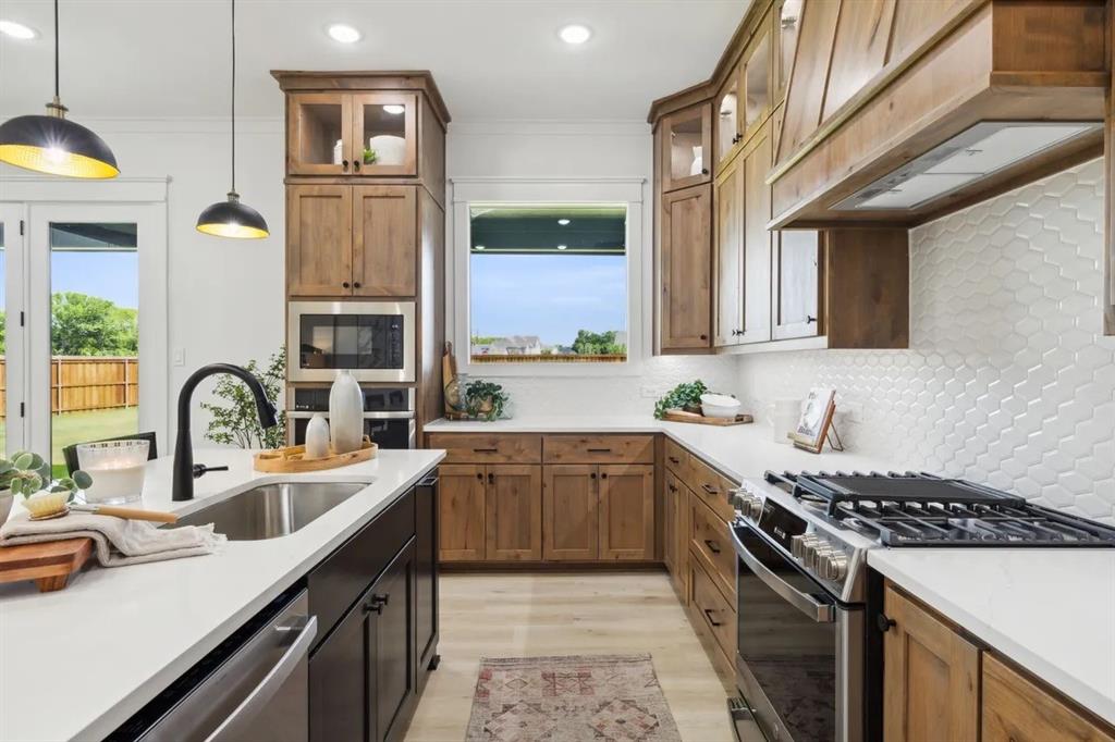 1310 Benjamin Trail Van Alstyne, TX 75495 - Photo 7 of 27 Kitchen with stainless steel appliances, glass insert cabinets, hanging light fixtures, two tone cabinets, and light wood-style flooring