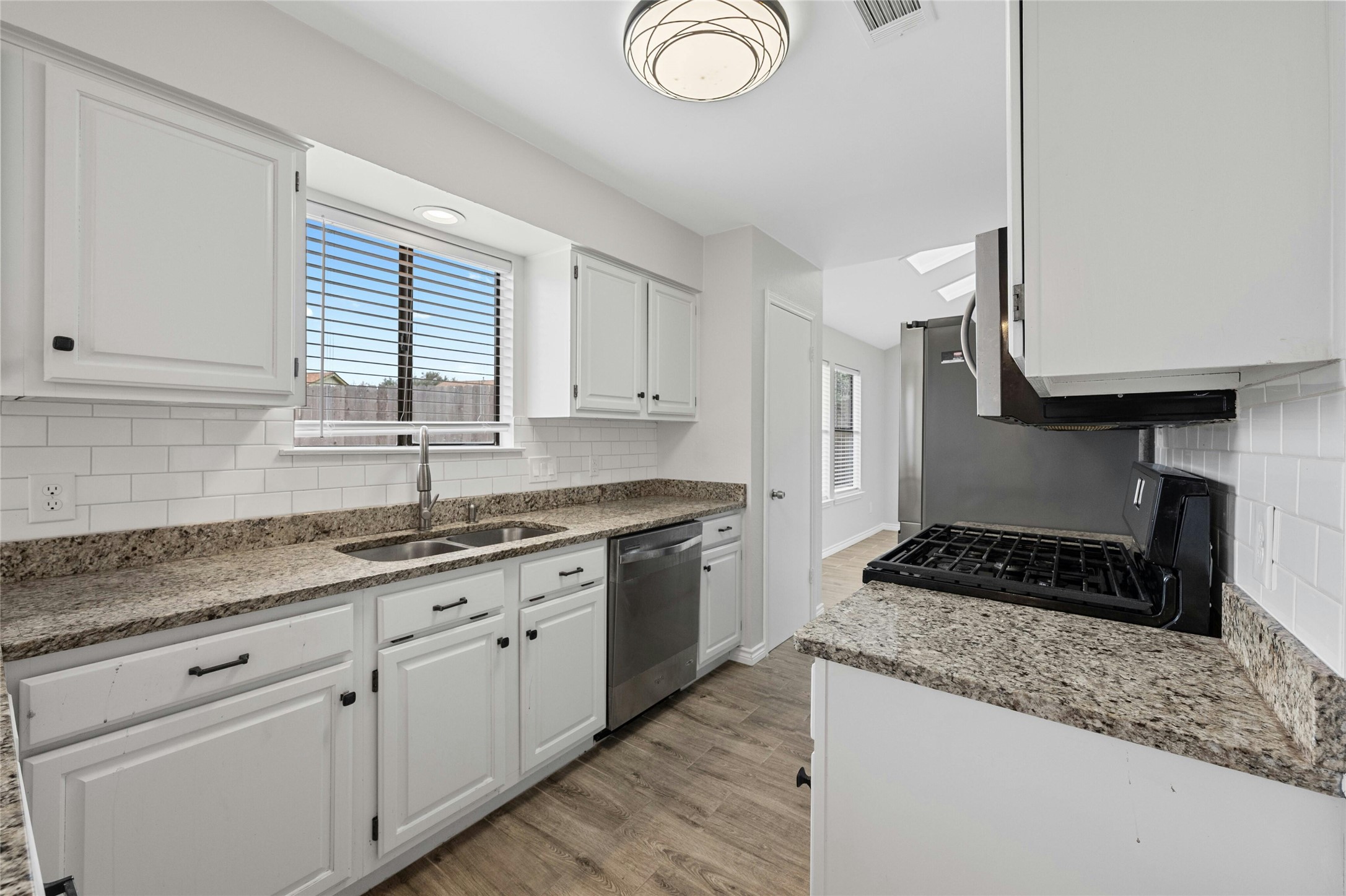 8303 Los Ranchos Drive Austin, TX 78749 - Photo 10 of 26 Kitchen featuring light wood-style flooring, white cabinetry, light stone countertops, decorative backsplash, and healthy amount of natural light
