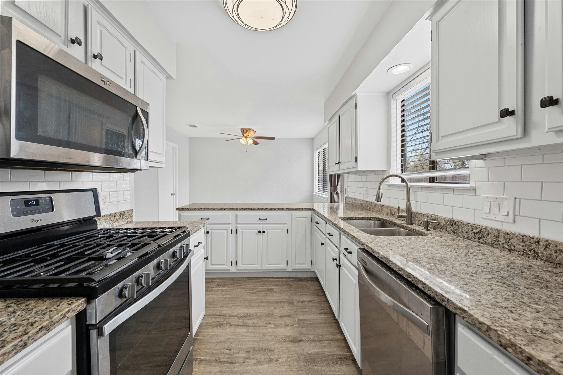 8303 Los Ranchos Drive Austin, TX 78749 - Photo 11 of 26 Kitchen with stainless steel appliances, light stone counters, white cabinetry, light wood-style floors, and a peninsula