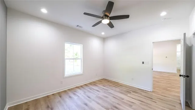 an empty room with wooden floor a ceiling fan and windows