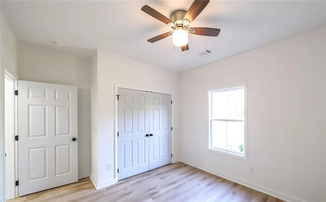 an empty room with wooden floor ceiling fan and windows