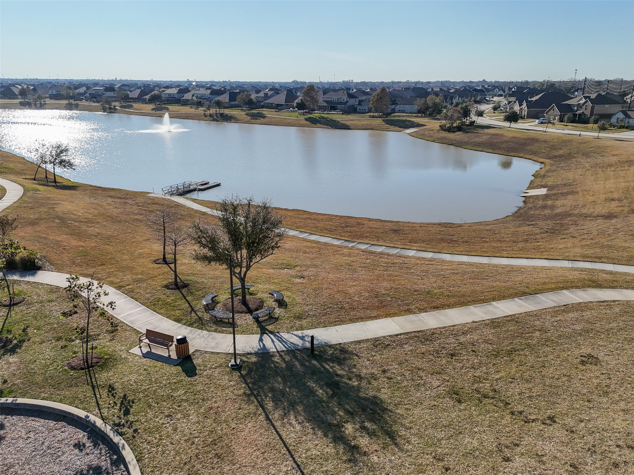 4747 Abercorn Street Rosharon, TX 77583 - Photo 43 of 46 This serene photo showcases a lake pond with a fountain, surrounded by paved walking paths and open grassy areas. The neighborhood in the background adds to the community feel, making it an ideal spot for relaxation or a leisurely stroll.