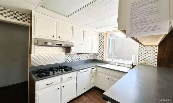 a kitchen with granite countertop a stove a sink dishwasher and white cabinets with wooden floor