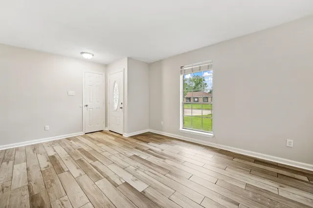 a view of an empty room with wooden floor and a window