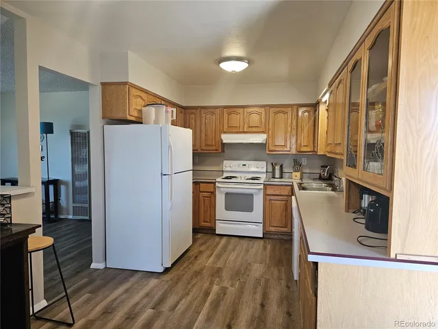 a kitchen with a refrigerator a stove top oven a sink dishwasher and wooden cabinets with wooden floor