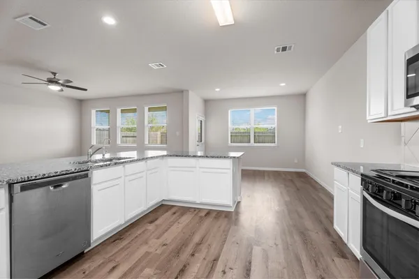 a kitchen with granite countertop a stove a sink wooden floor and cabinets