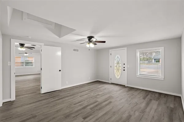 an empty room with wooden floor chandelier fan and windows