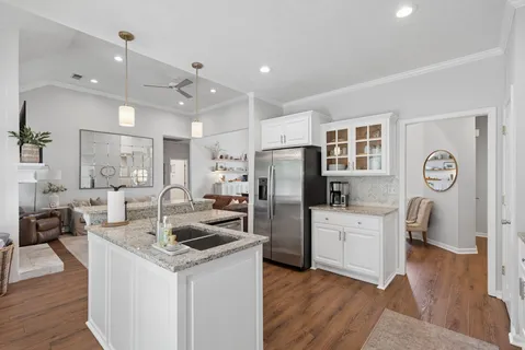 a living room with stainless steel appliances kitchen island granite countertop a refrigerator a stove top oven a sink dishwasher and wooden cabinets with wooden floor
