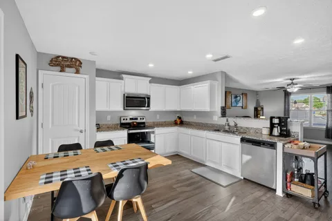 a kitchen with stainless steel appliances granite countertop a stove top oven a sink dishwasher and white cabinets with wooden floor