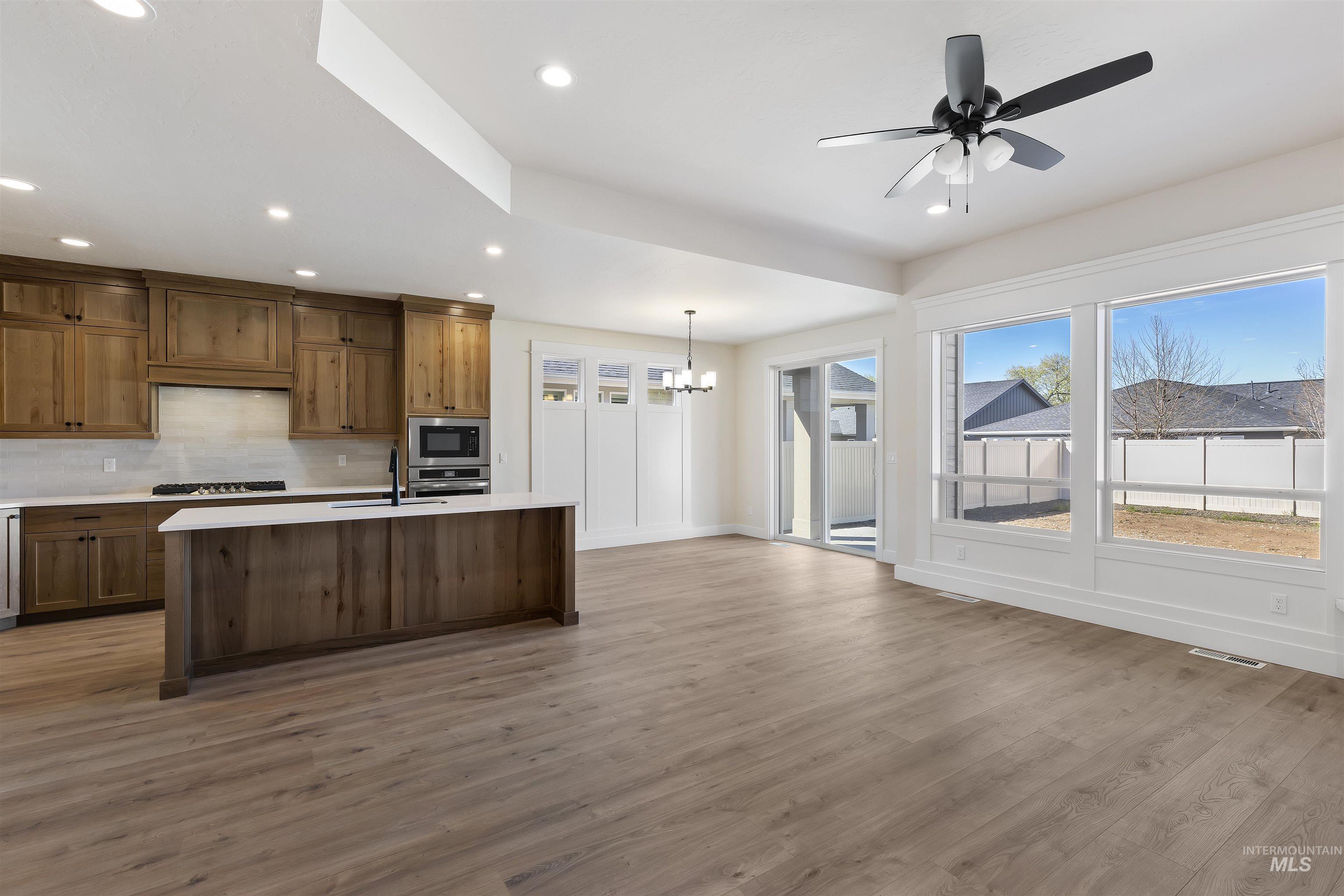 3501 South El Rio Avenue Boise, ID 83709 - Photo 13 of 31 Kitchen featuring ceiling fan, decorative backsplash, light wood finished floors, a center island with sink, and a chandelier