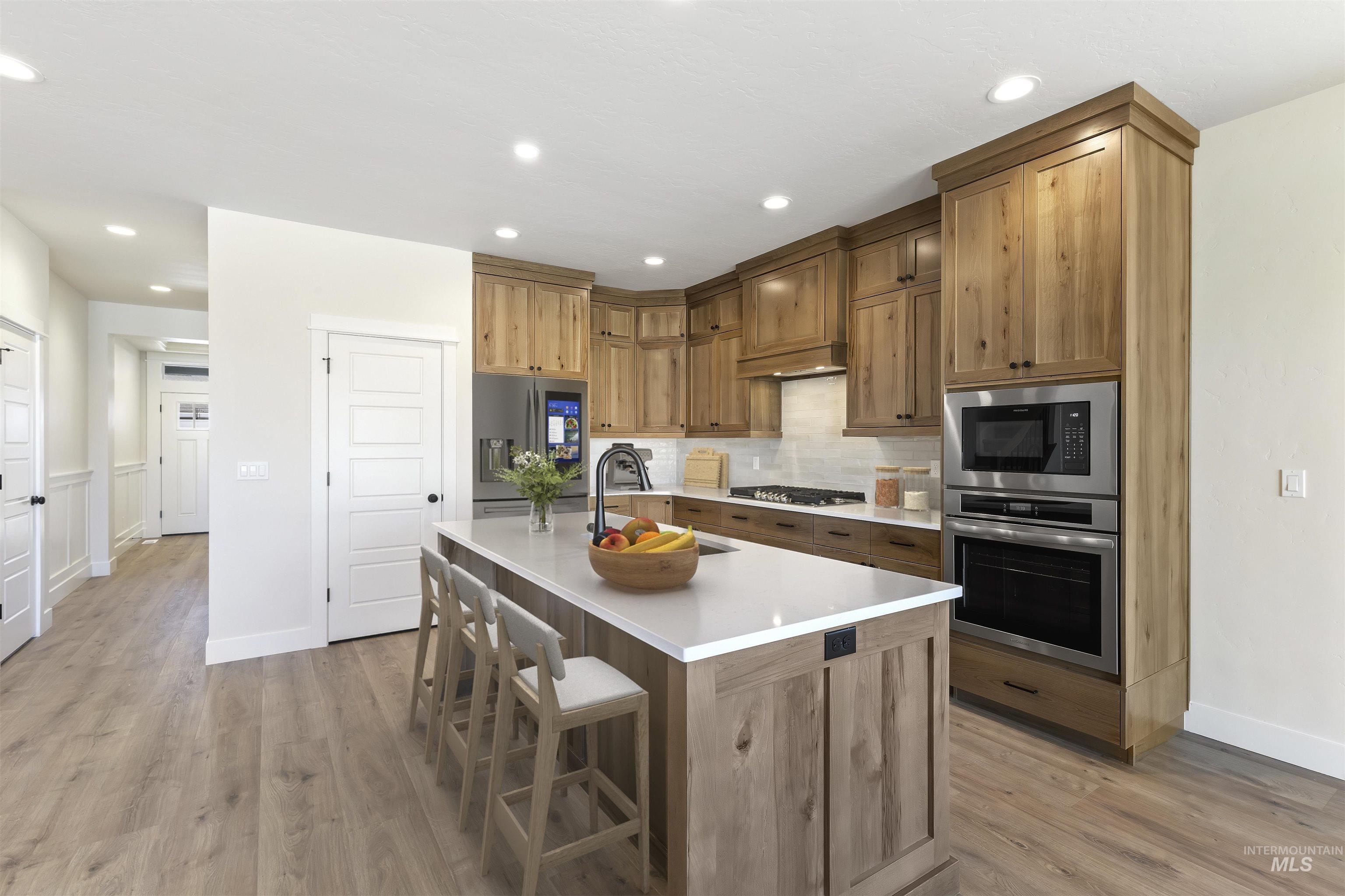 3501 South El Rio Avenue Boise, ID 83709 - Photo 5 of 31 Kitchen featuring stainless steel appliances, light wood-type flooring, a center island with sink, a kitchen bar, and backsplash