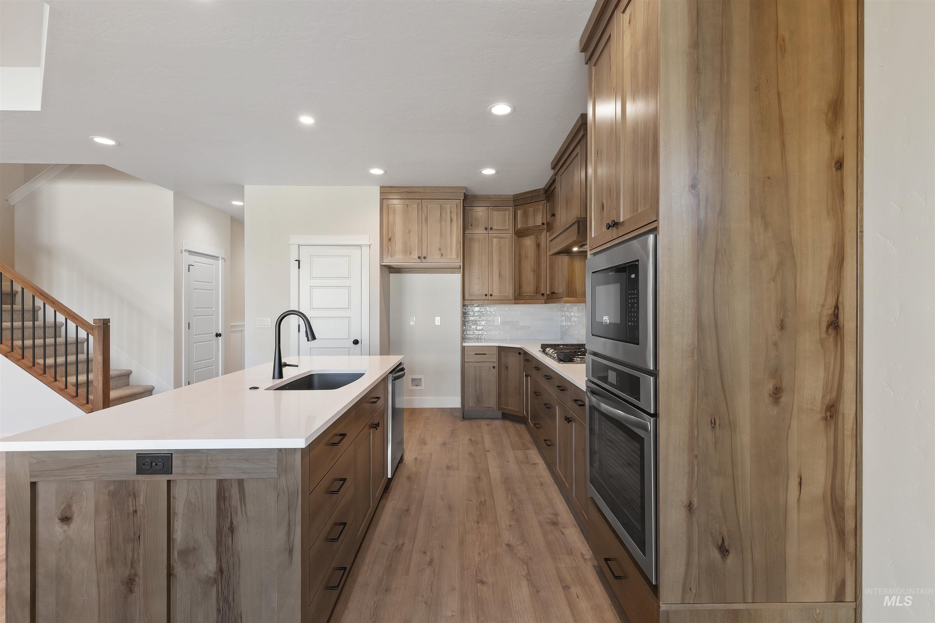 3501 South El Rio Avenue Boise, ID 83709 - Photo 6 of 31 Kitchen featuring stainless steel appliances, wood finish cabinets, a kitchen island with sink, light wood finished floors, and decorative backsplash