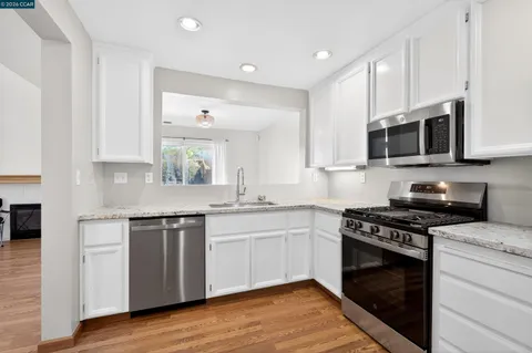 a kitchen with stainless steel appliances granite countertop a stove top oven a sink dishwasher and a microwave oven with wooden floor