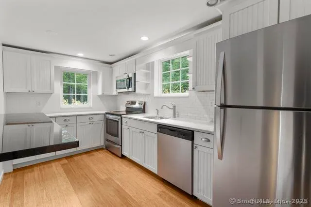 a kitchen with stainless steel appliances granite countertop a refrigerator a sink dishwasher a stove and white countertops with wooden floor