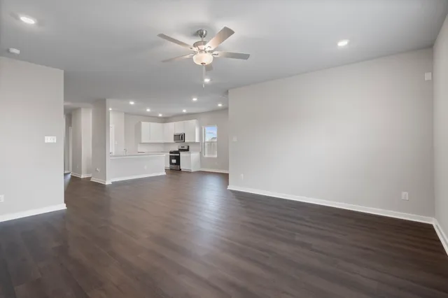 a view of an empty room and kitchen with wooden floor